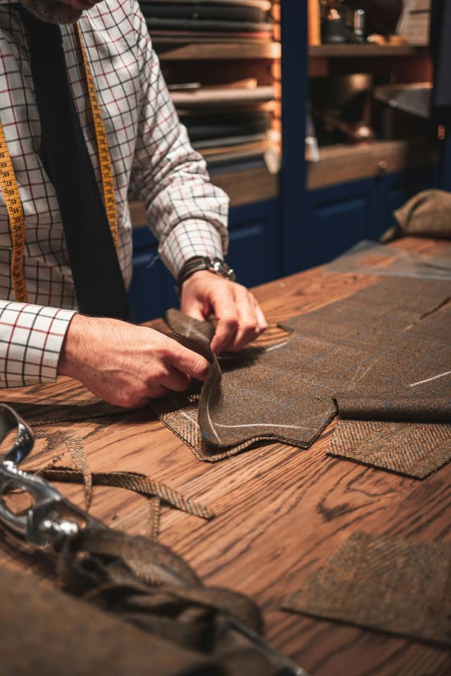 A tailor smoothing cut pattern pieces across a wooden bench